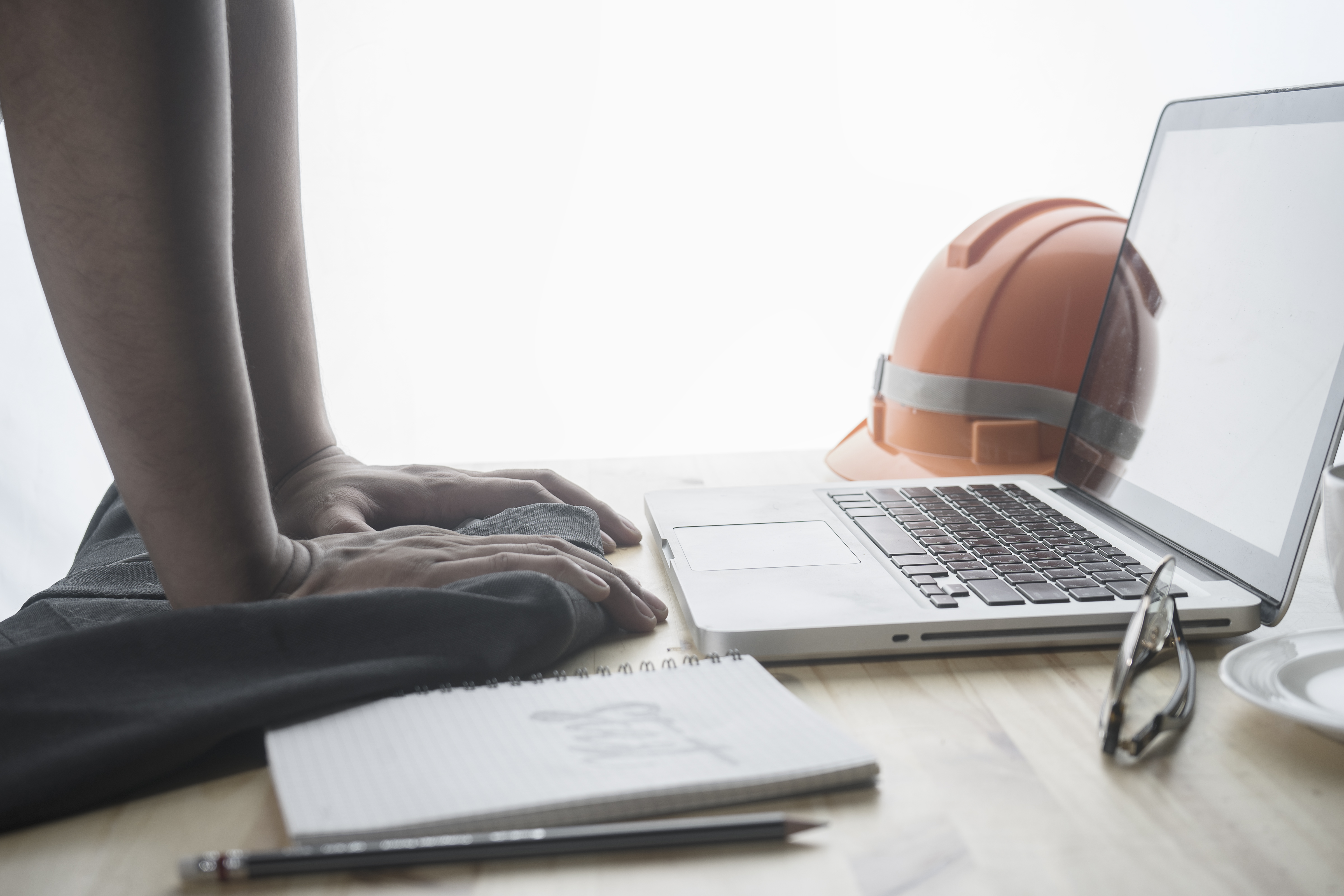 Picture of a hard hat, laptop, and hands on a table