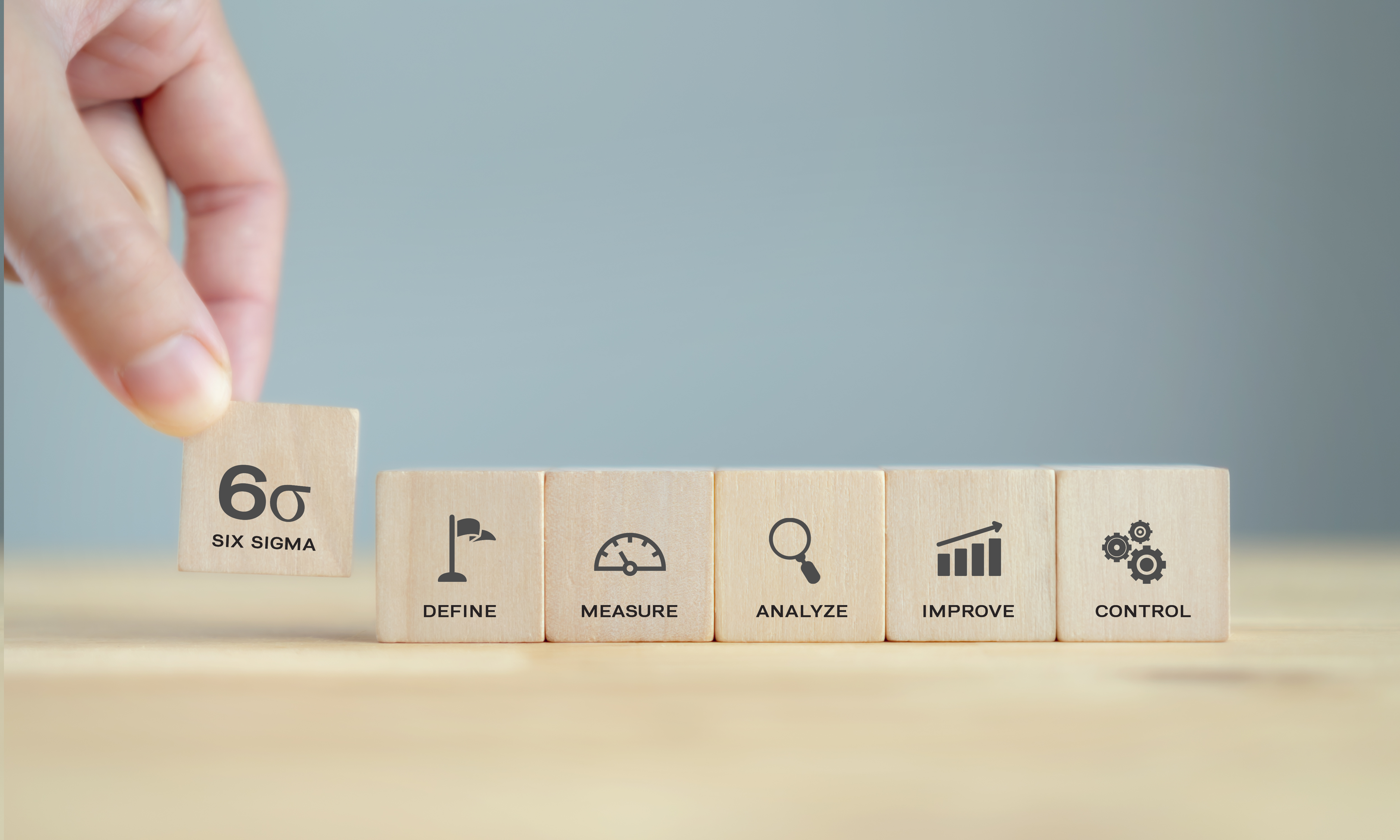 Hand placing wooden block in row of business-icon blocks on gray background