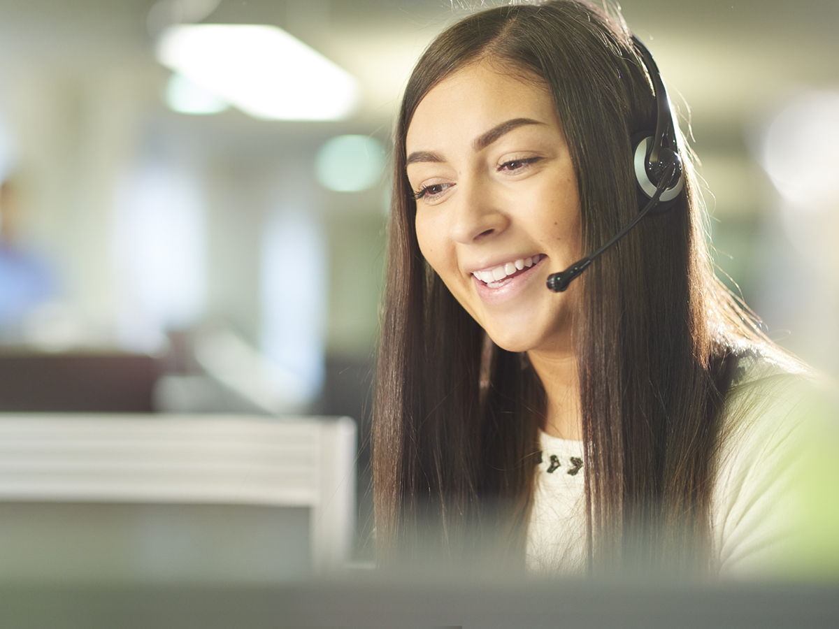 a woman with a phone headset on smiles while talking 