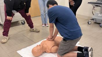 A medical practitioner looks on as pre-college students practice CPR on a dummy during their field trip to UC Davis Emergency Medicine Department