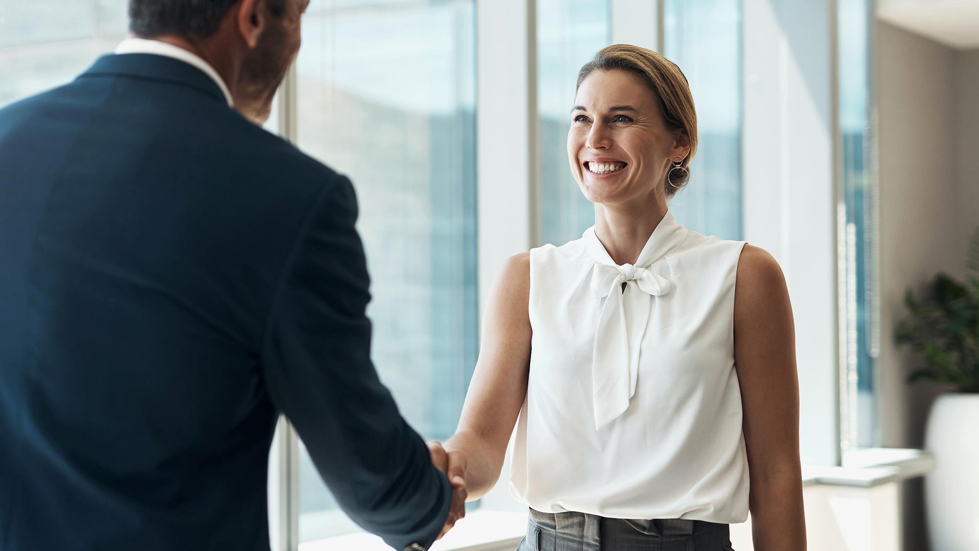 man in suit shaking hands with woman in office
