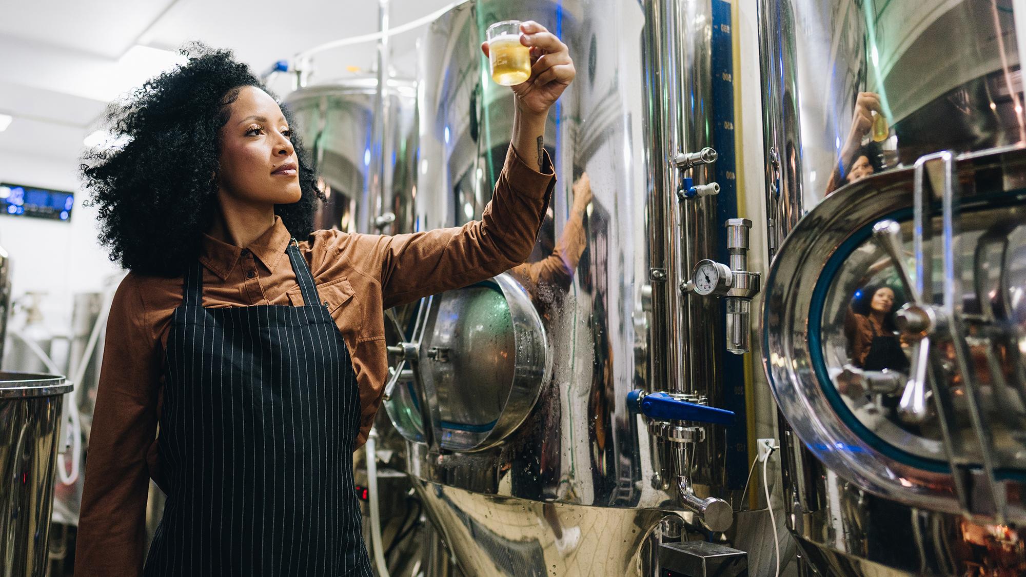 woman in apron examining a glass of beer
