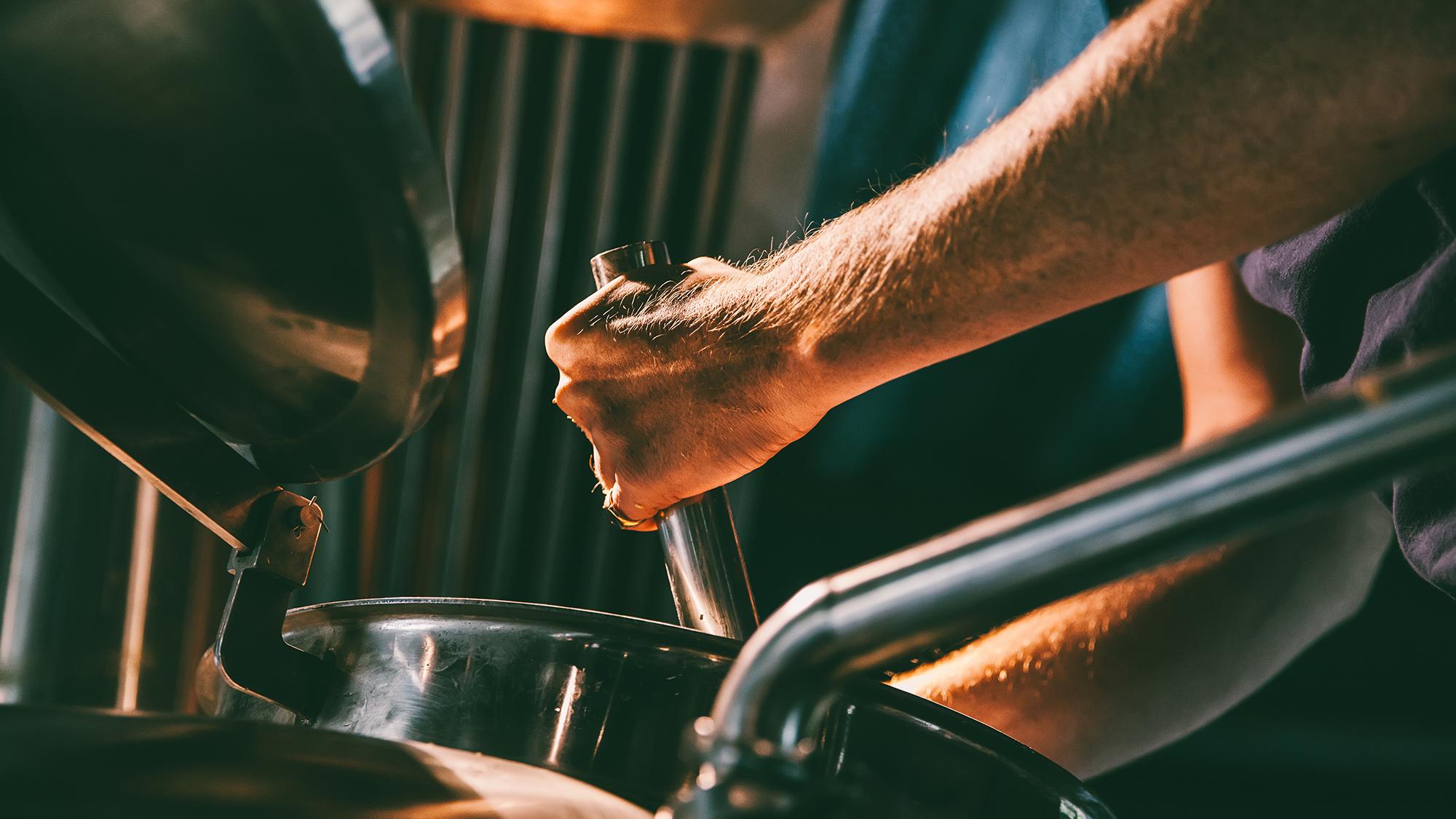 man's hands stirring beer in industrial brewing equipment