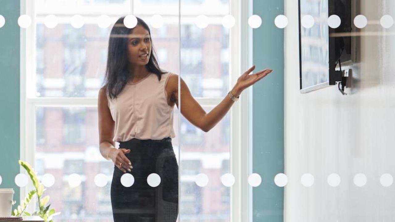 woman pointing to whiteboard as colleagues watch from conference table