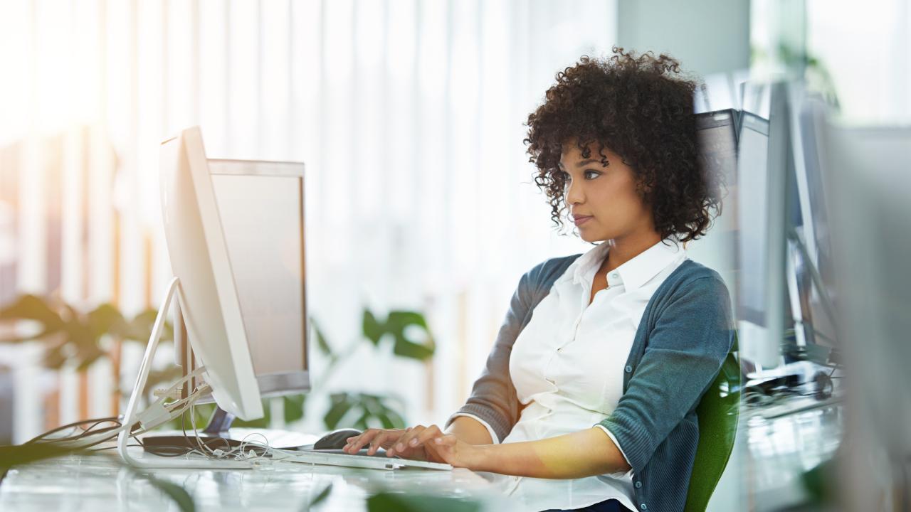 Curly-haired woman working at a desktop computer in a bright modern office