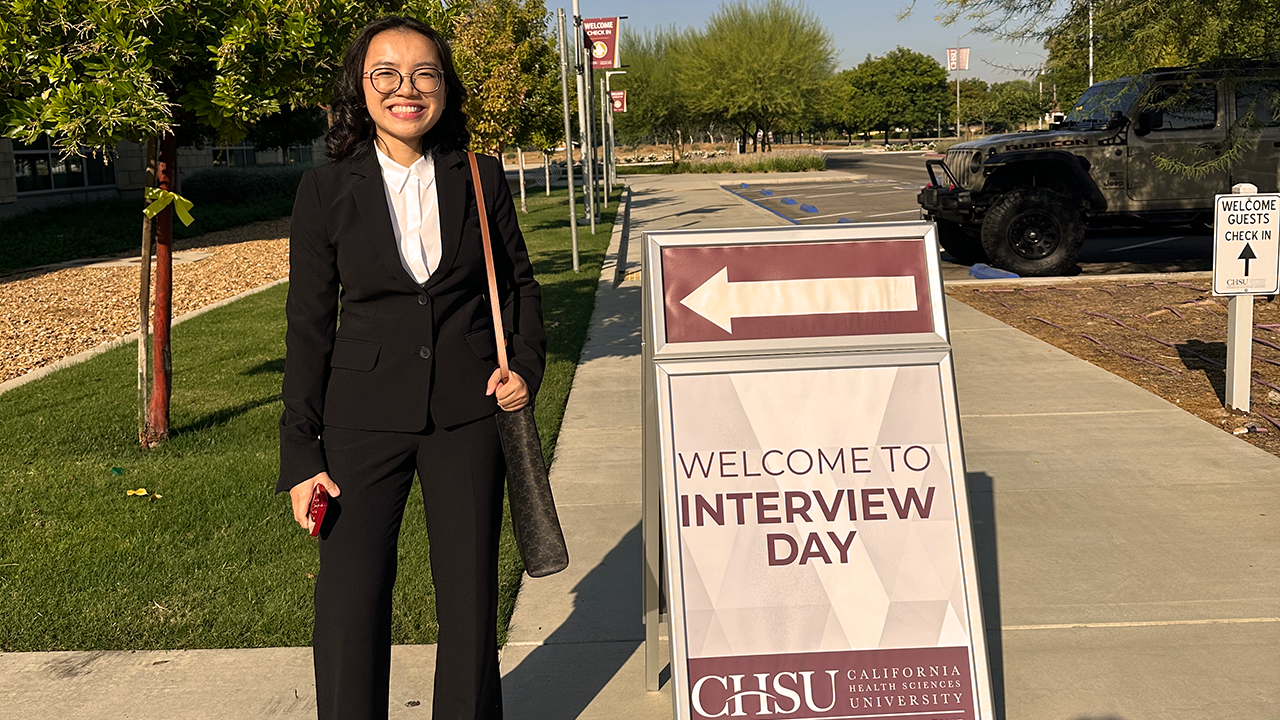 Smiling woman in black suit beside sidewalk sign reading 'Welcome to Interview Day' and arrow