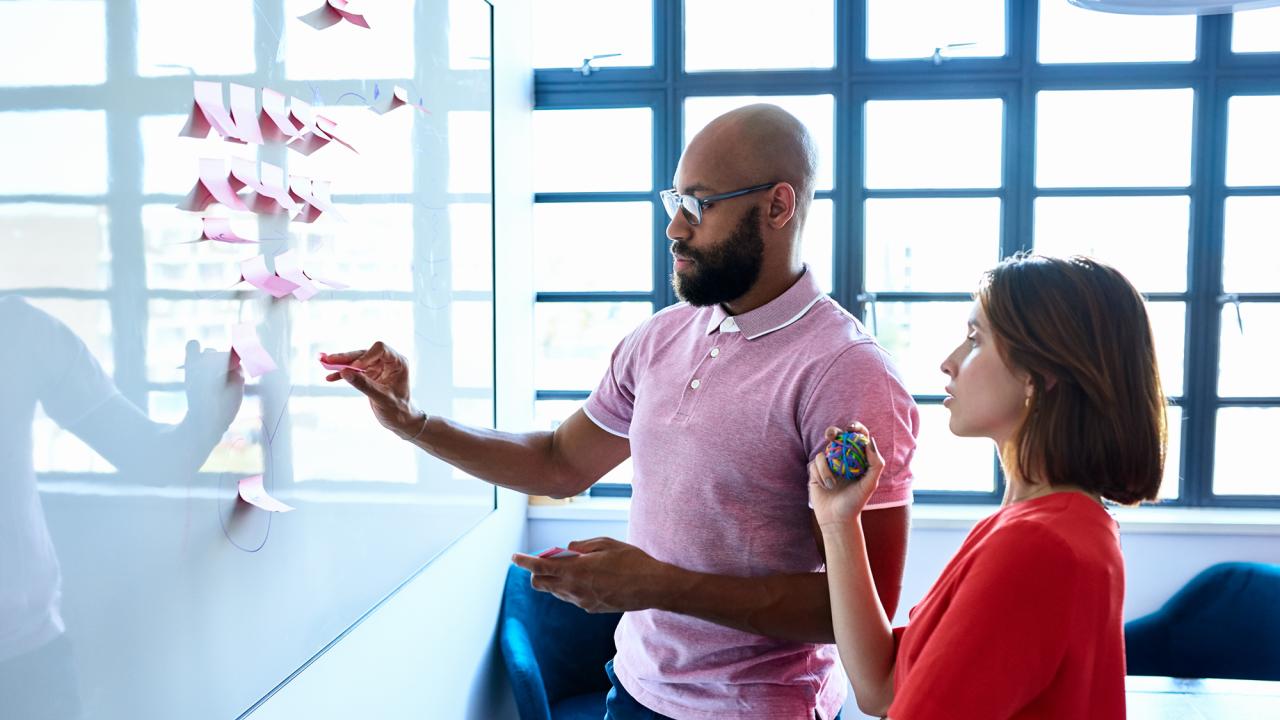 male and female colleague write ideas on sticky notes