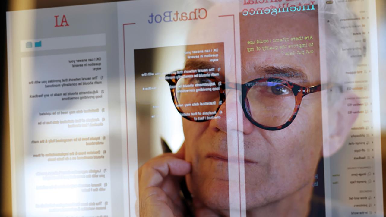 Close up photograph of a mature man studying a see-through computer monitor that’s displaying text provided by AI 