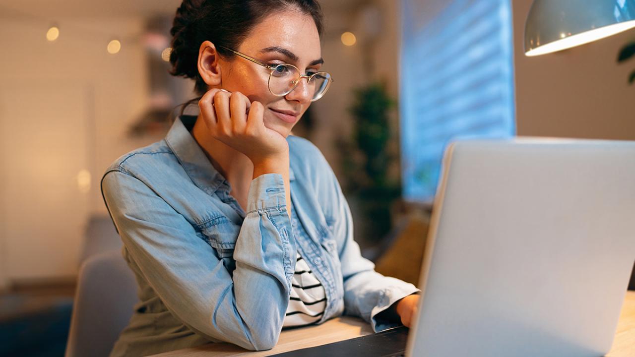 a woman at home sits at a desk looking at her laptop