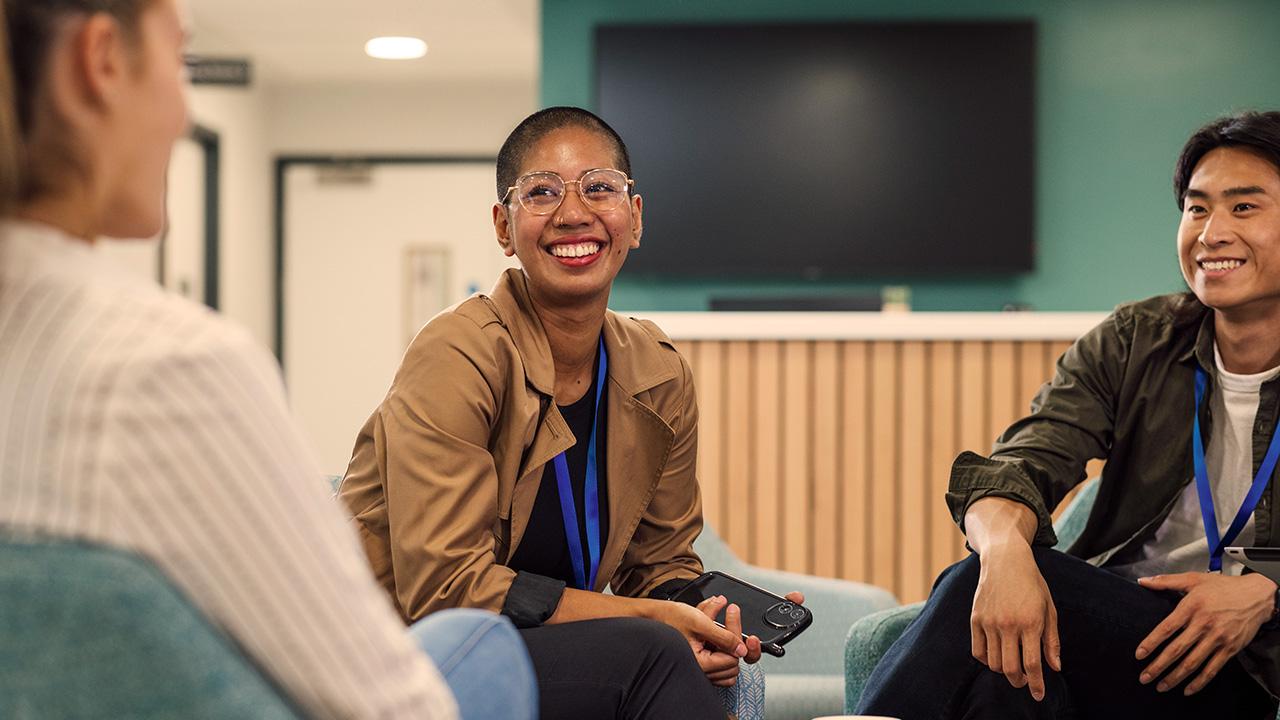 Three colleagues smiling and talking in a modern office lounge