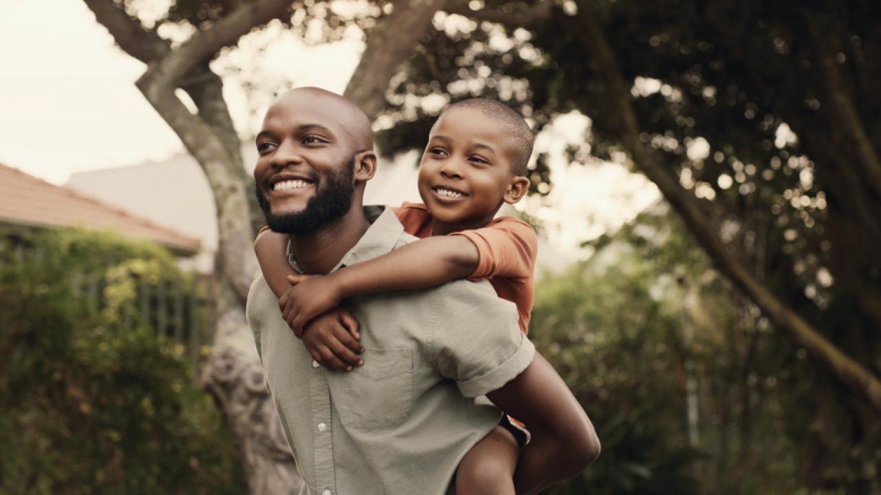 African American man carrying young son on his shoulders, both are smiling