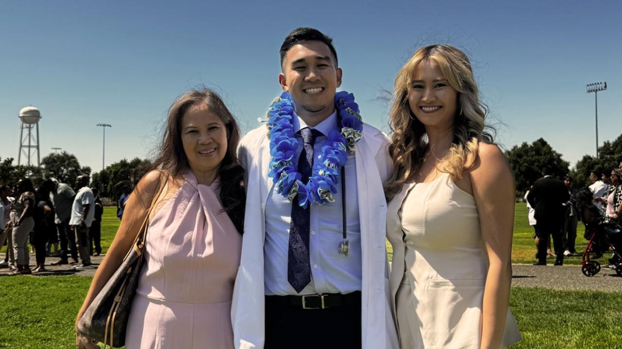 UC Davis Health Professions Post-bac grad J.T. poses in his white coat with his mom and sister