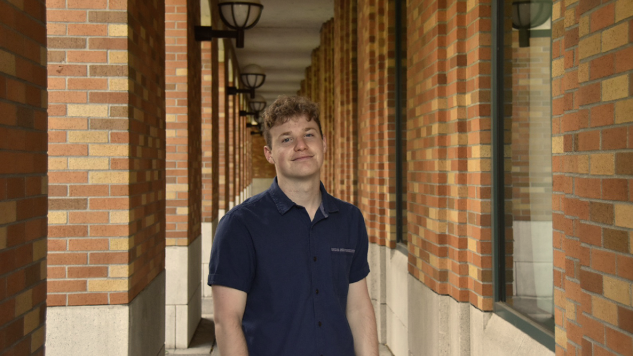 Smiling young man in navy shirt standing in brick-columned corridor