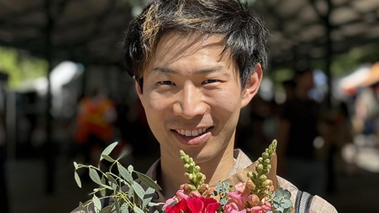 UC Davis GSP graduate Ryotaro Okada poses with flowers at the Davis Farmer's Market