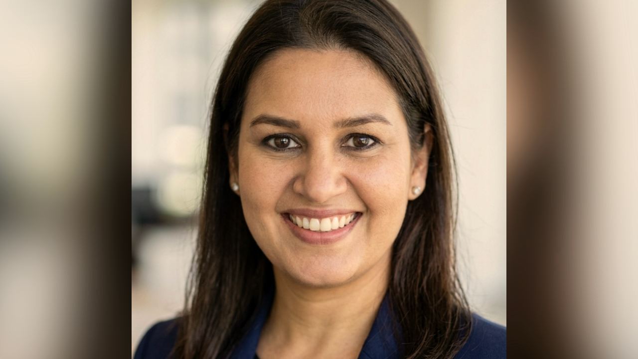 Smiling professional headshot of a dark-haired woman, blurred office background