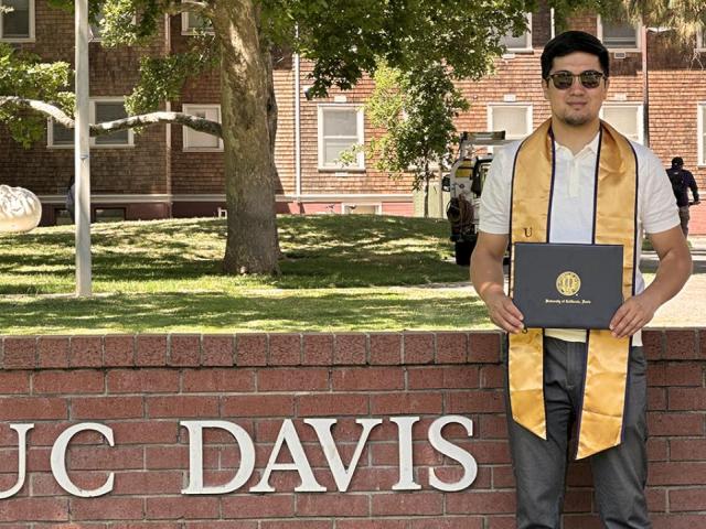 Zhankeldy Doszhanov standing in front of a UC Davis sign with his diploma