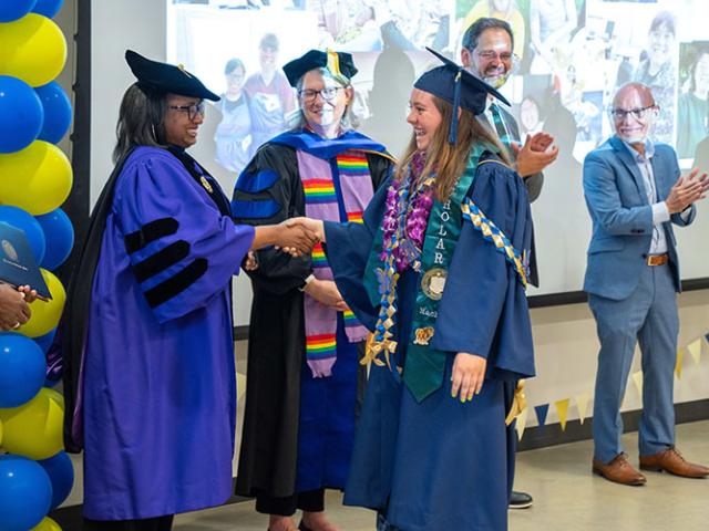 From left, Chancellor Gary S. May looks on as Renetta Garrison Tull shakes hands with scholar Rachel Holt at the graduation on June 7. Also pictured are Dean of Continuing and Professional Education Julie Greenwood, Director of Access Programs at Continuing and Professional Education Jake Hosier, Distinguished Professor Emeritus of Psychiatry and Behavioral Sciences and former MIND Institute Director Leonard Abbeduto and Redwood SEED Employment Director Maddi Hinchey.