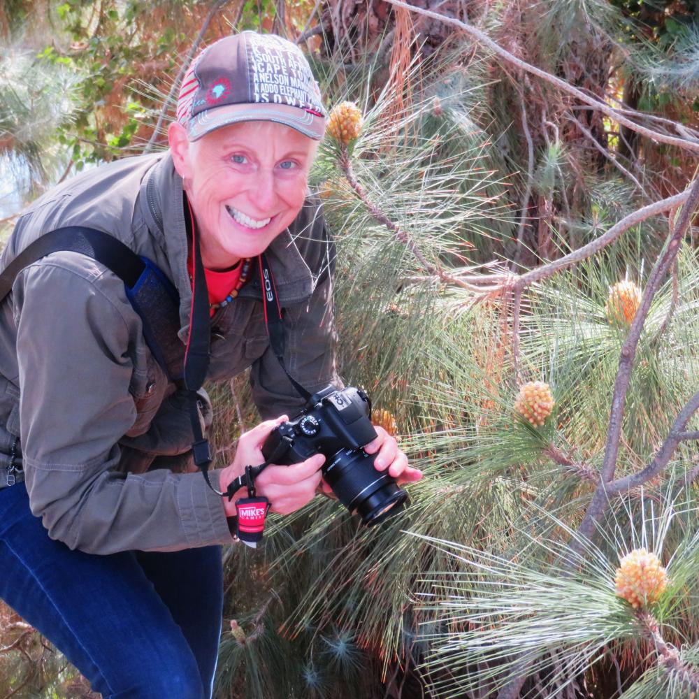 A man with a camera outdoors, smiling.