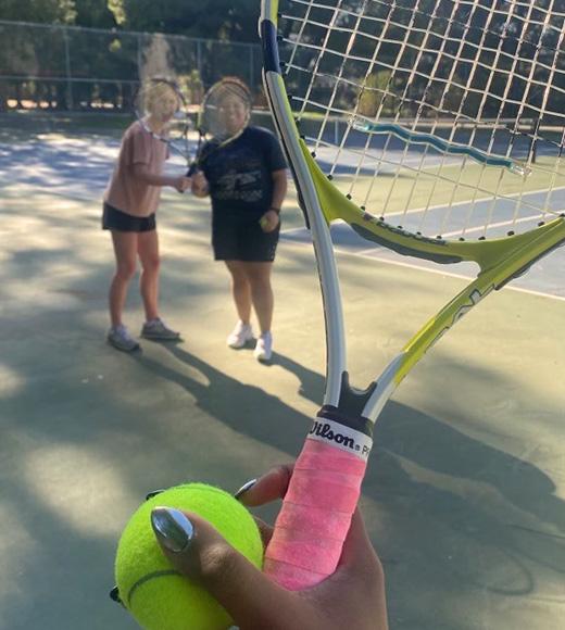 close up of a tennis rack and ball with two women in the background