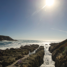 Sunlit rocky coastline with waves, cliffs, and a clear blue sky