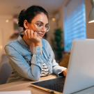 a woman at home sits at a desk looking at her laptop