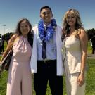 UC Davis Health Professions Post-bac grad JT poses in his white coat with his mom and sister