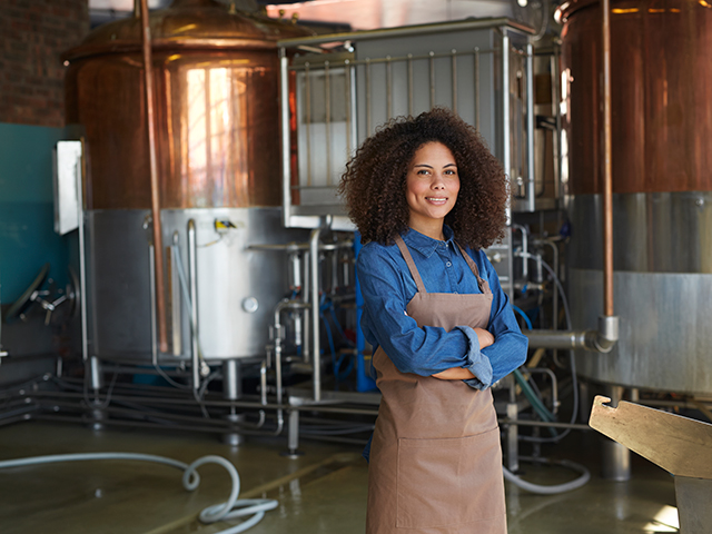 woman wearing apron standing in front of brewing equipment