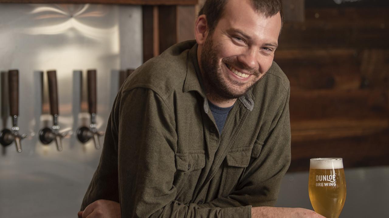 Brennan Fleming, photographed inside his Davis brewery, Dunloe Brewing. (Karin Higgins/UC Davis) Brennan Fleming at his bar with beer