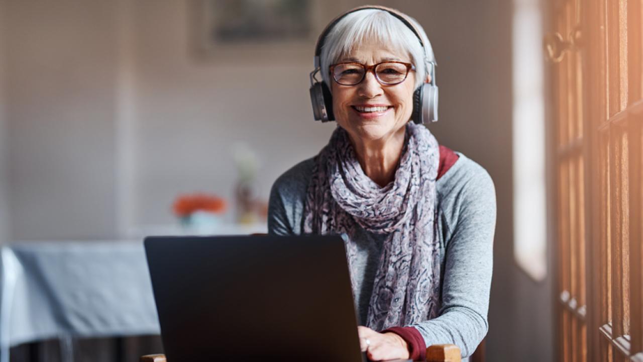 senior with headphones on at computer smiling