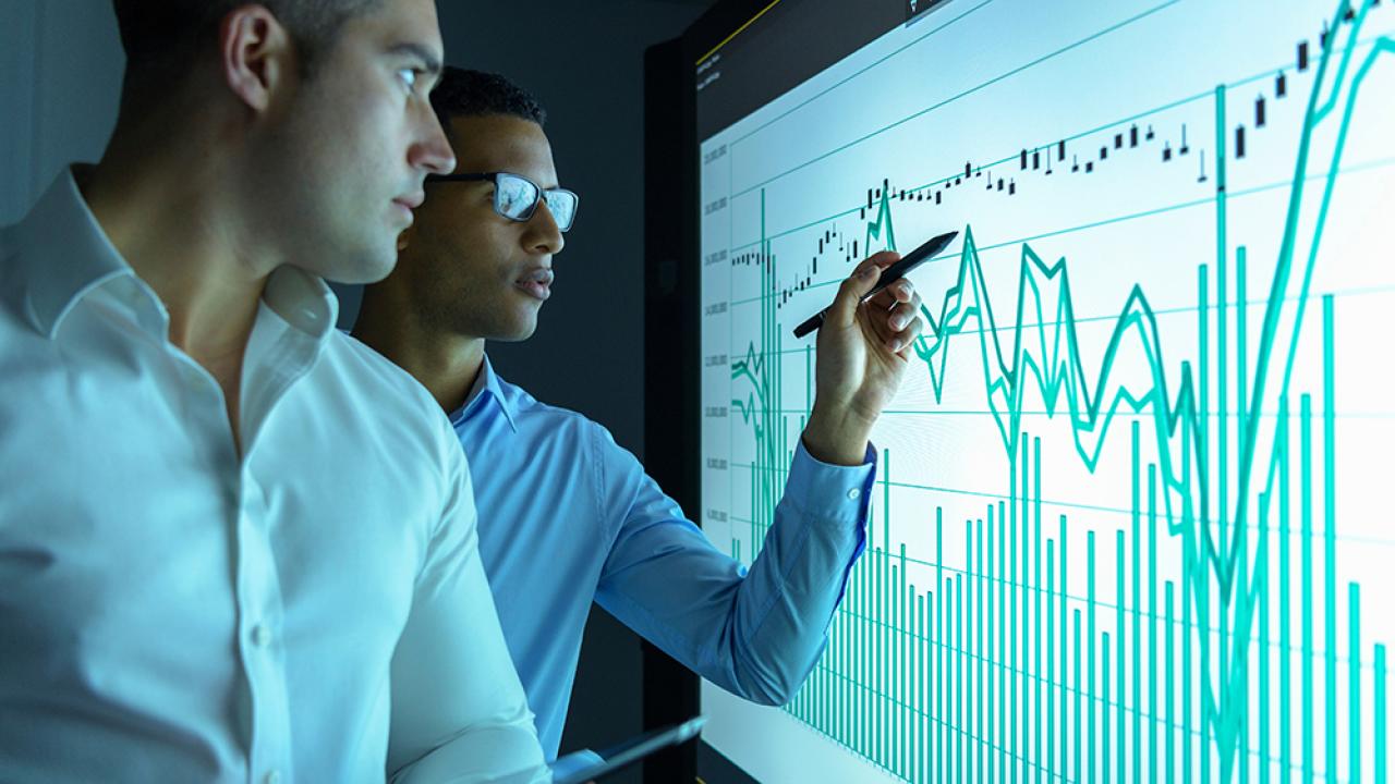 man watching another man pointing to a graph on a screen