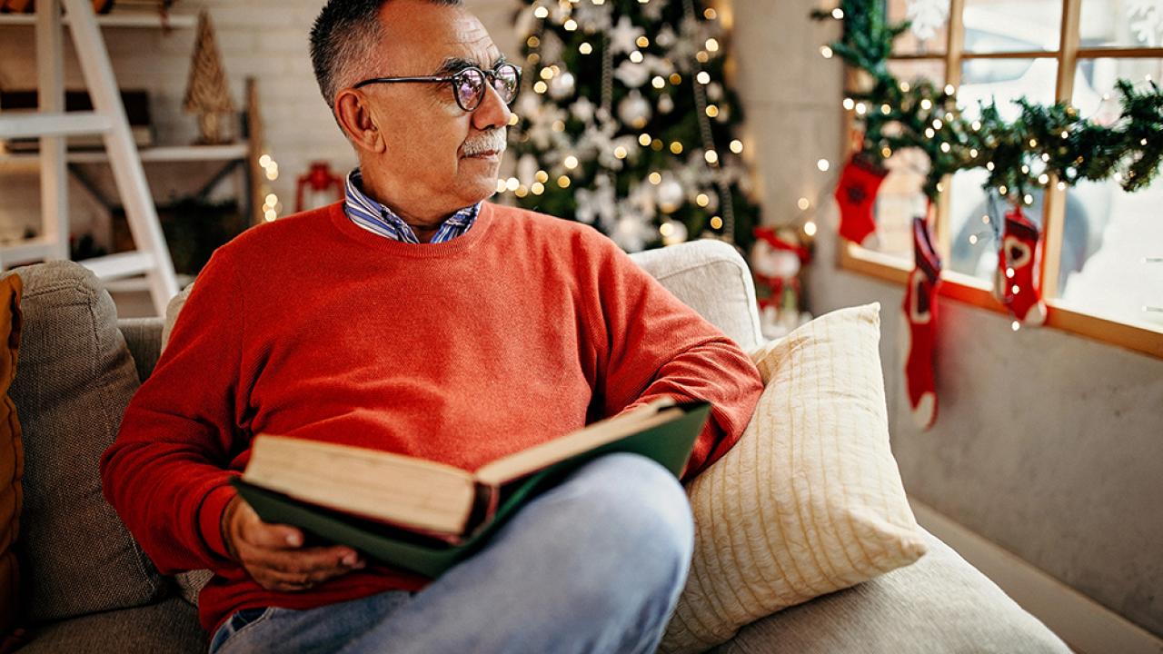 adult male senior reading book by Christmas tree