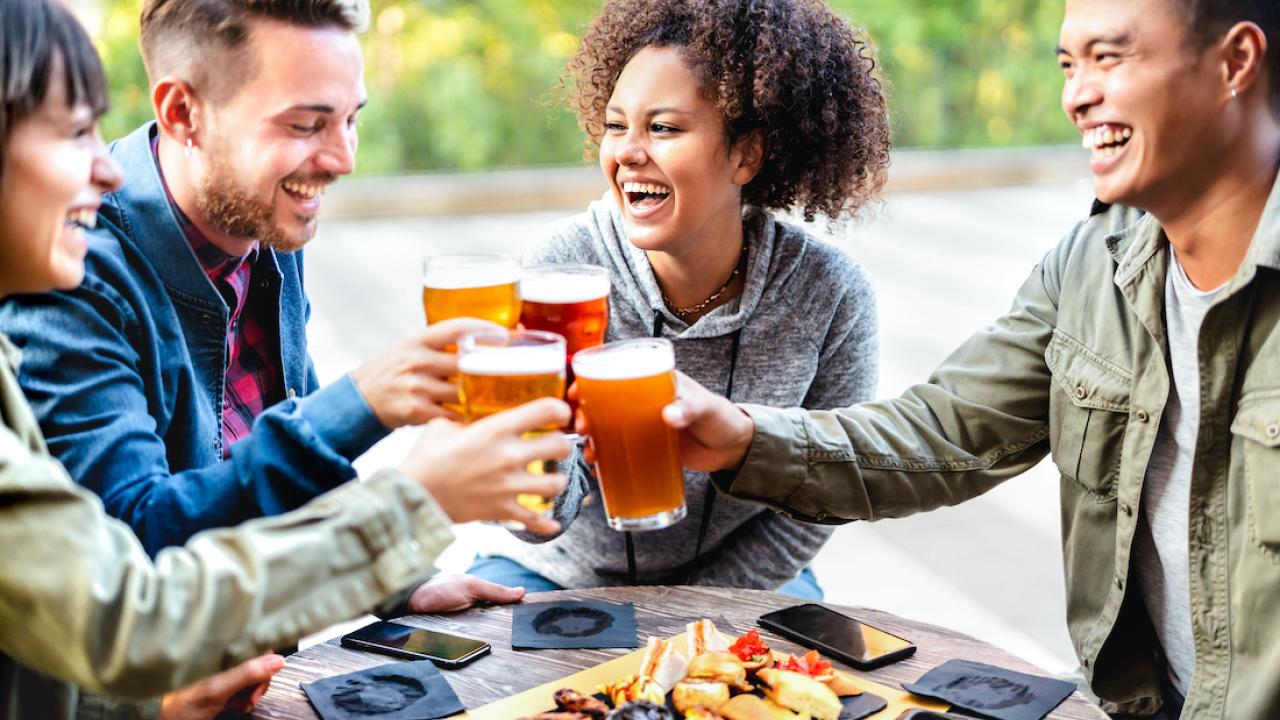 Friends make a toast with their beers at an outdoor restaurant.