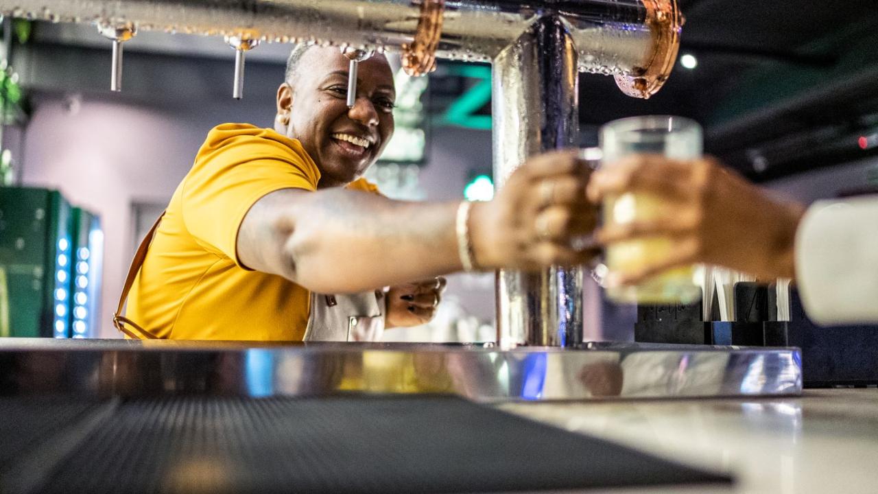 Bar tender smiling giving a drink to a customer or waiter.