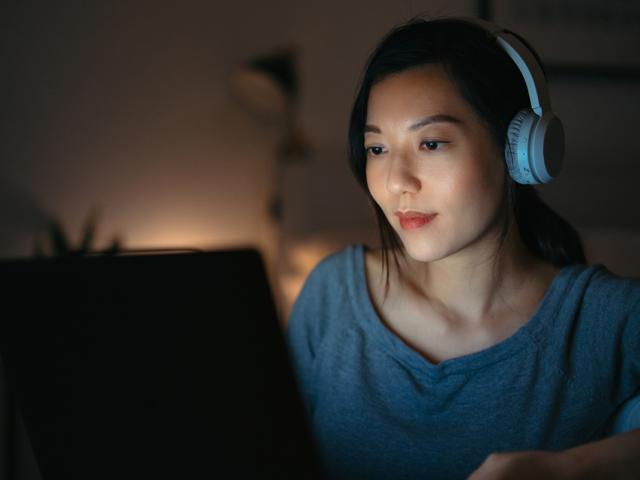 a woman sits at her laptop with headphones on