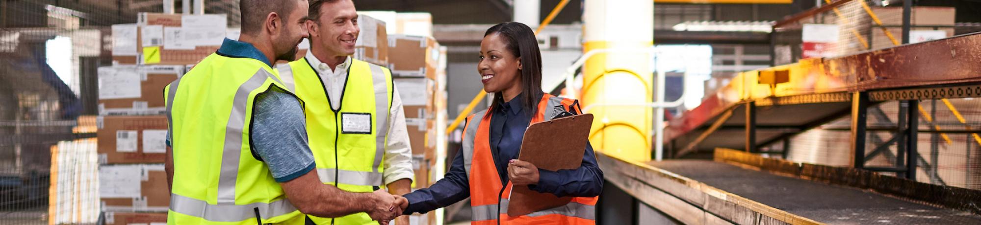 woman and men in safety vests talking and shaking hands in a warehouse